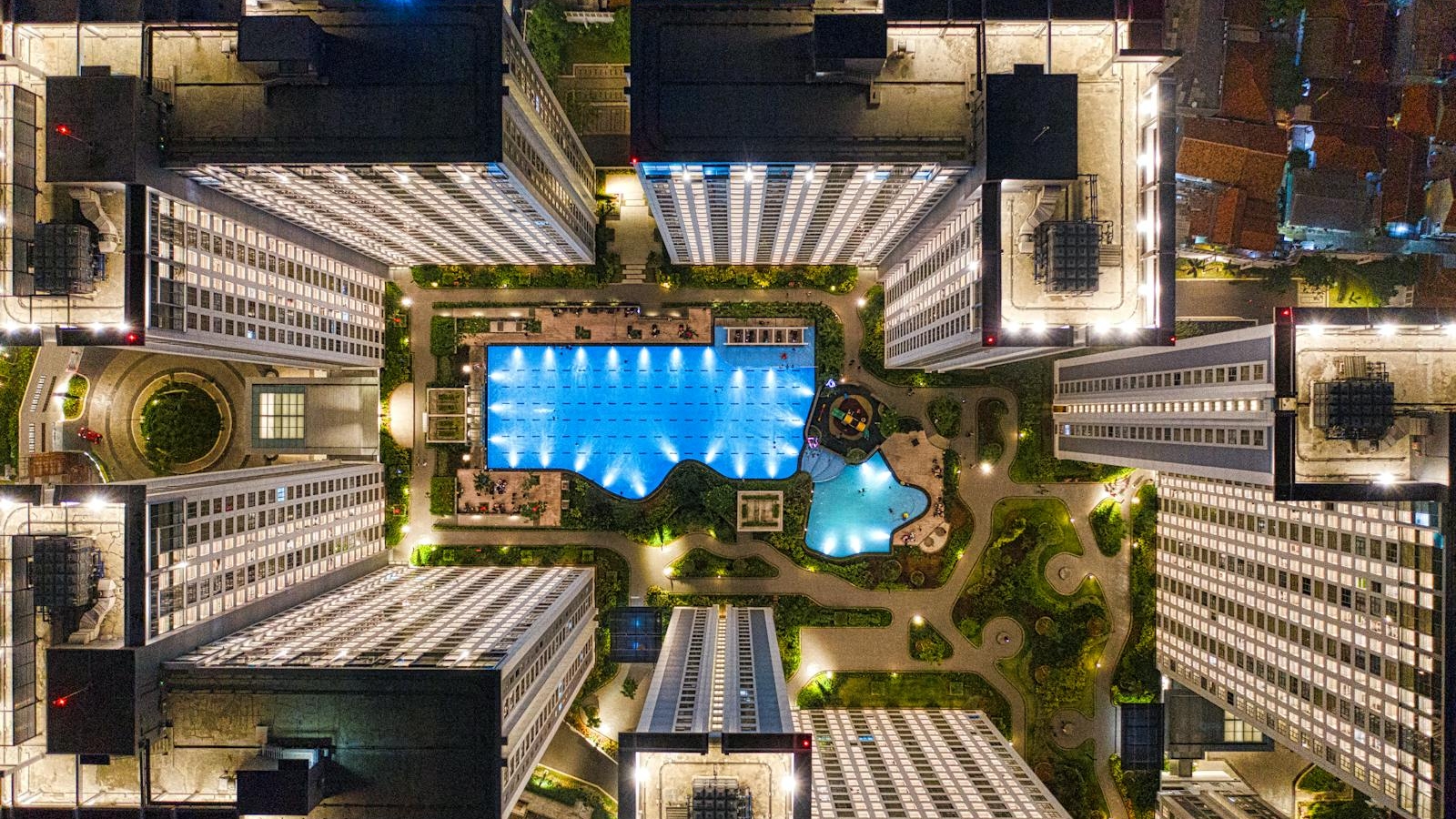 drone footage of illuminated modern urban complex with pool