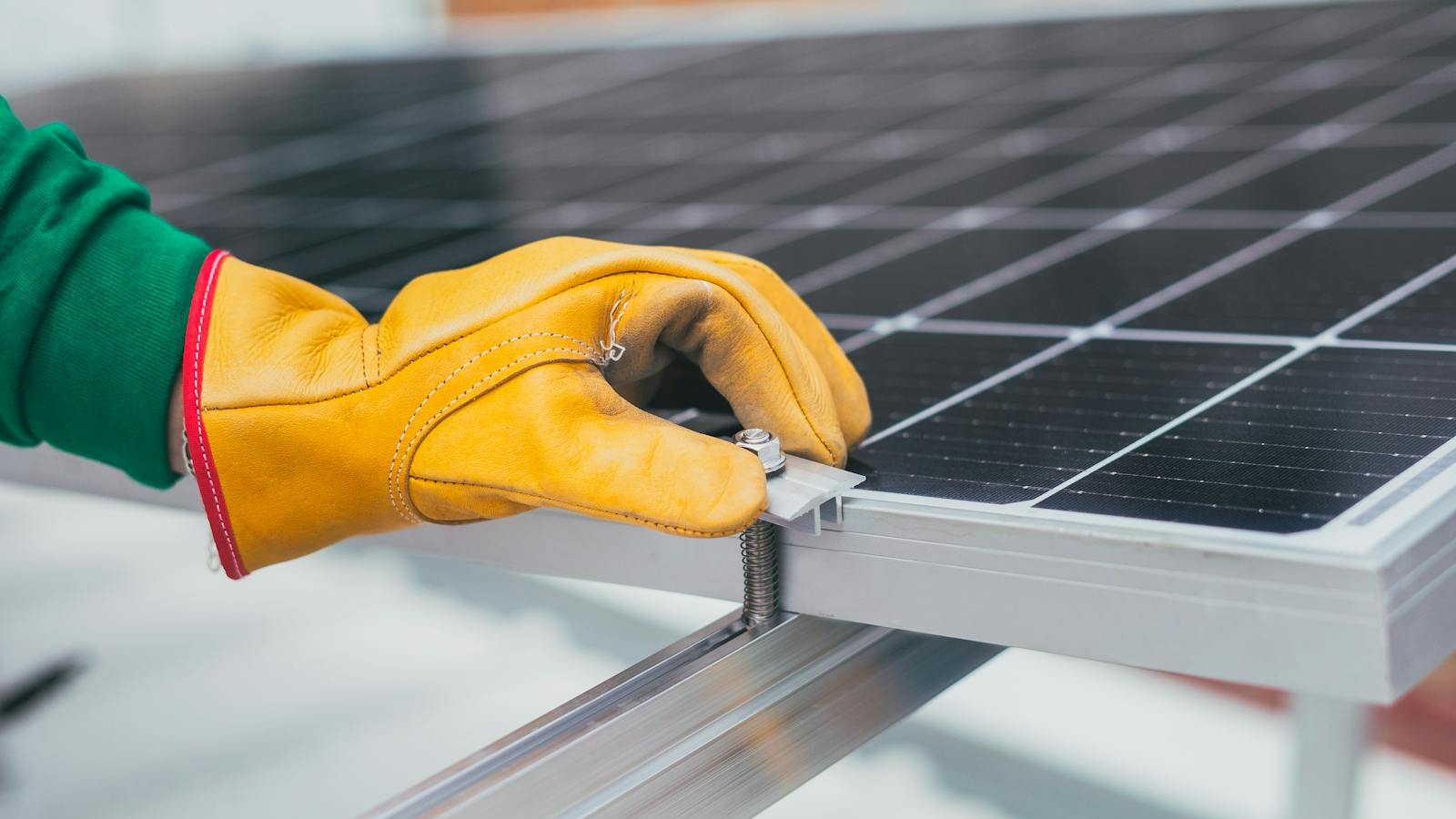 Close-up of a worker's hand with protective gloves adjusting a bolt on a solar panel.