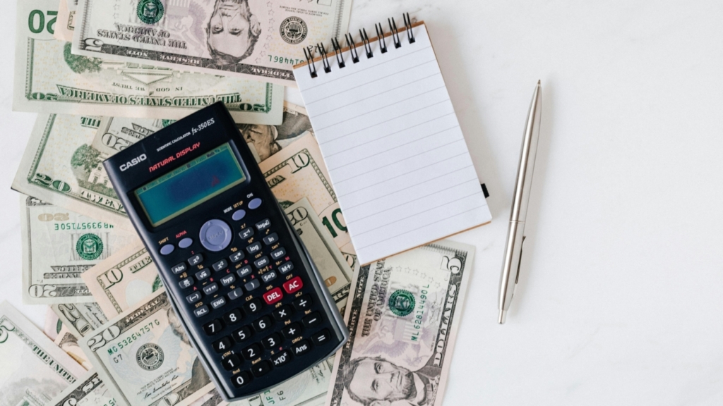 A calculator, a notepad, a pen and dollar bills