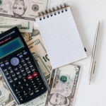 A calculator, a notepad, a pen and dollar bills
