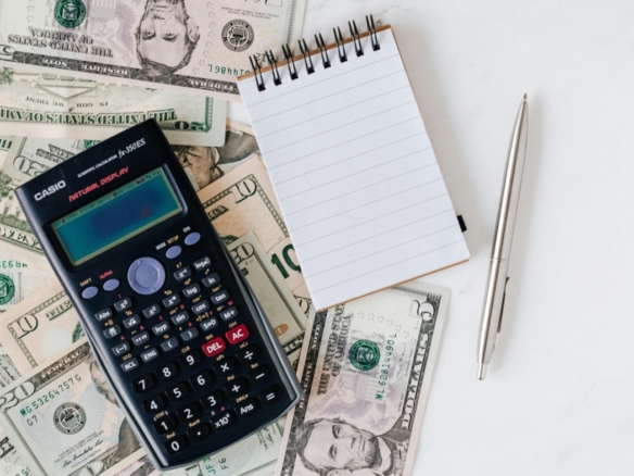 A calculator, a notepad, a pen and dollar bills