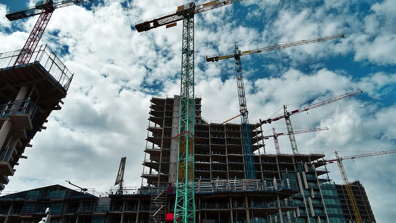 Urban construction site with numerous cranes framing rising skyscrapers against a blue sky.