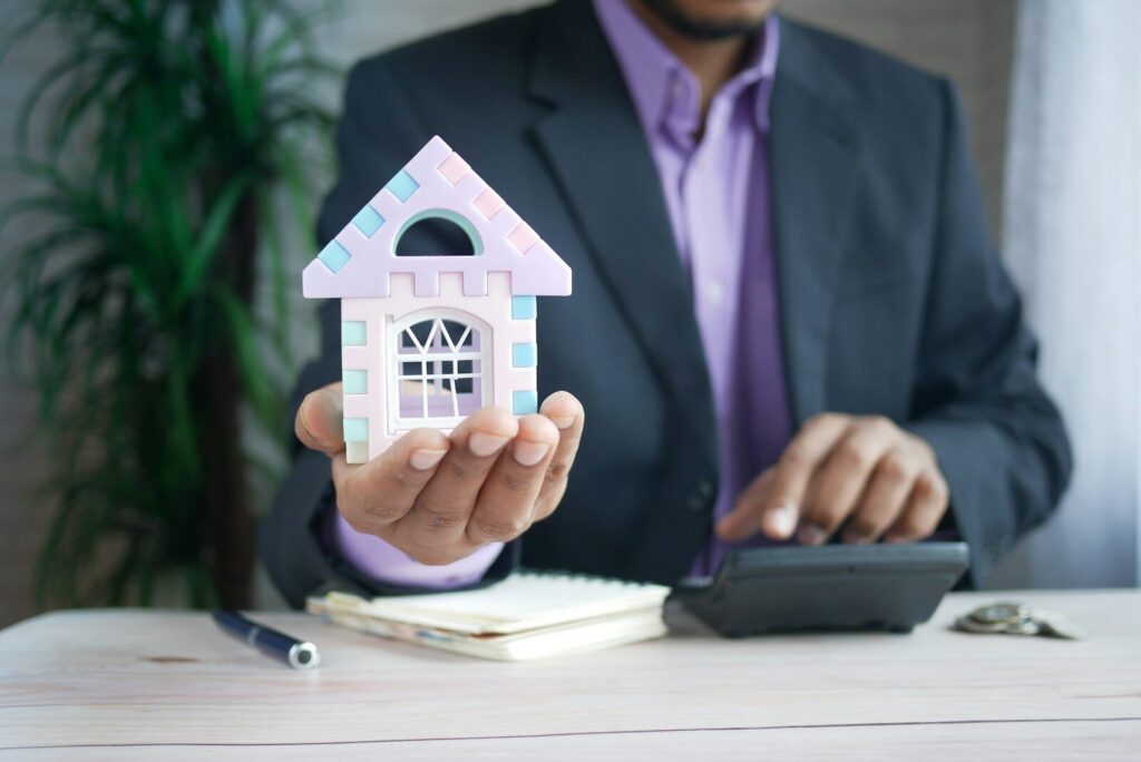 man holding model house at desk with calculator